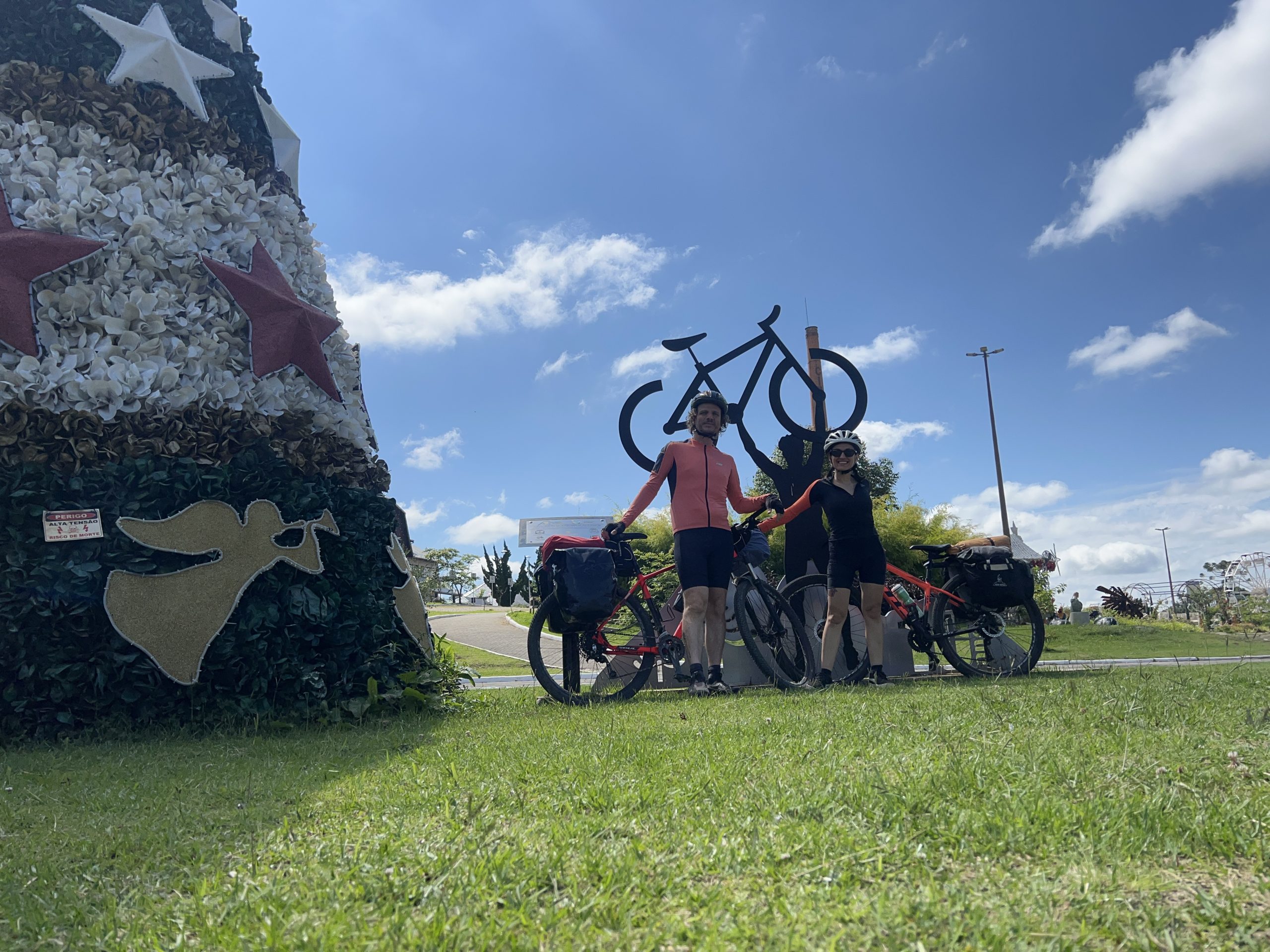 Casal ciclista posando em frente a escultura de bicicleta, início da jornada rumo à Patagônia