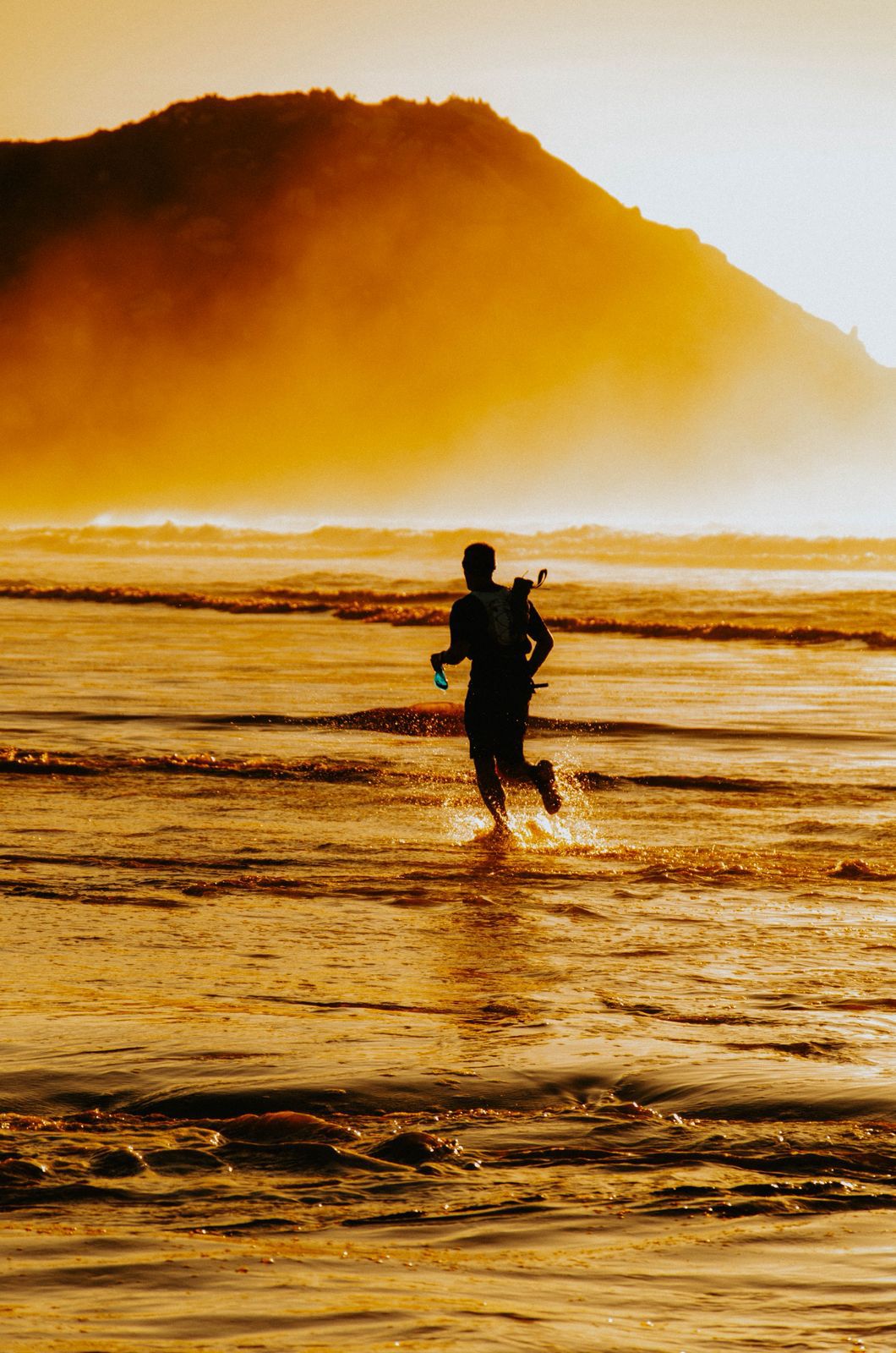 Corredor atravessa praia durante treino ao pôr do sol em cenário de montanha
