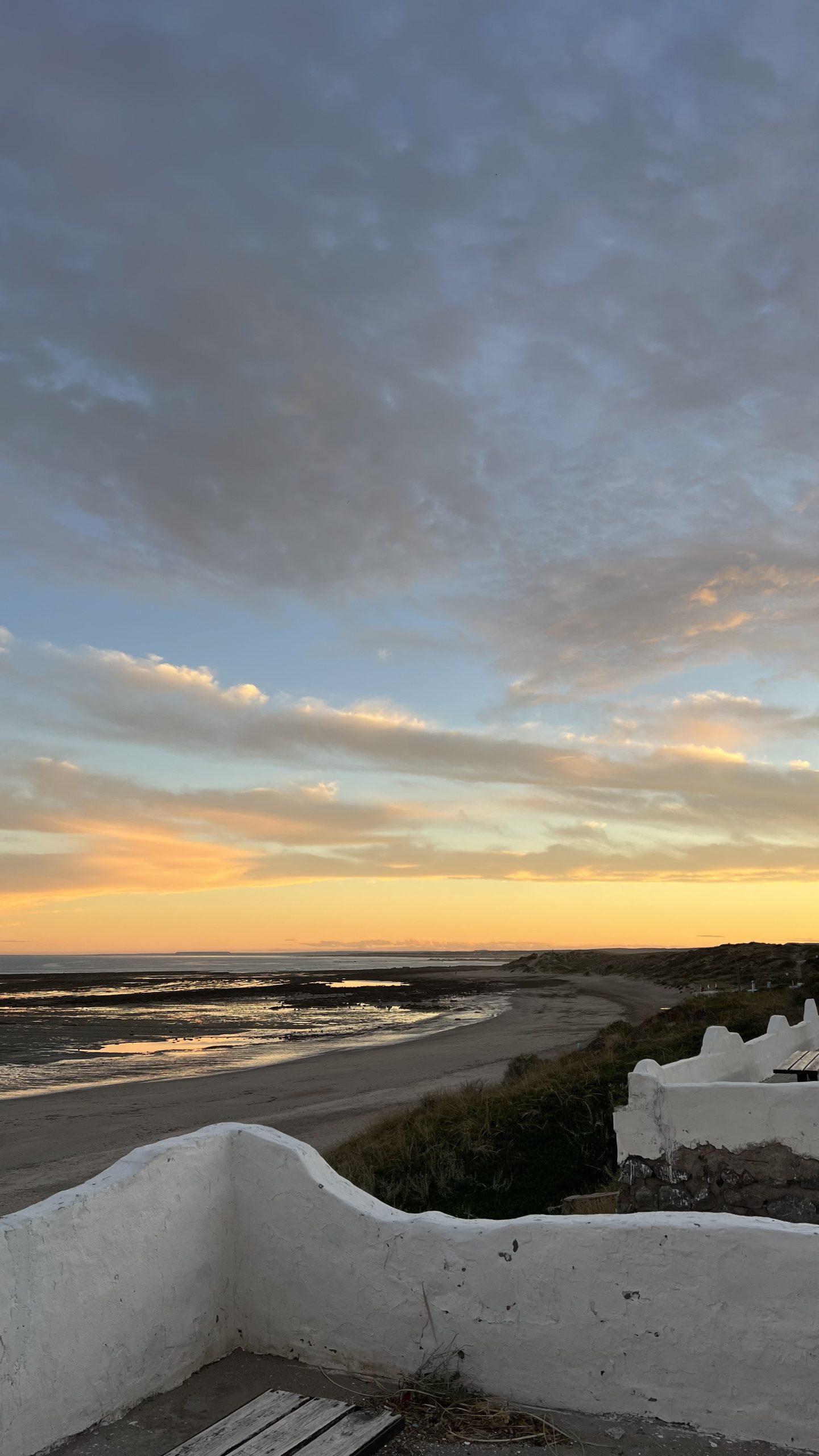Pôr do sol na praia de Las Grutas com mar calmo e falésias ao fundo