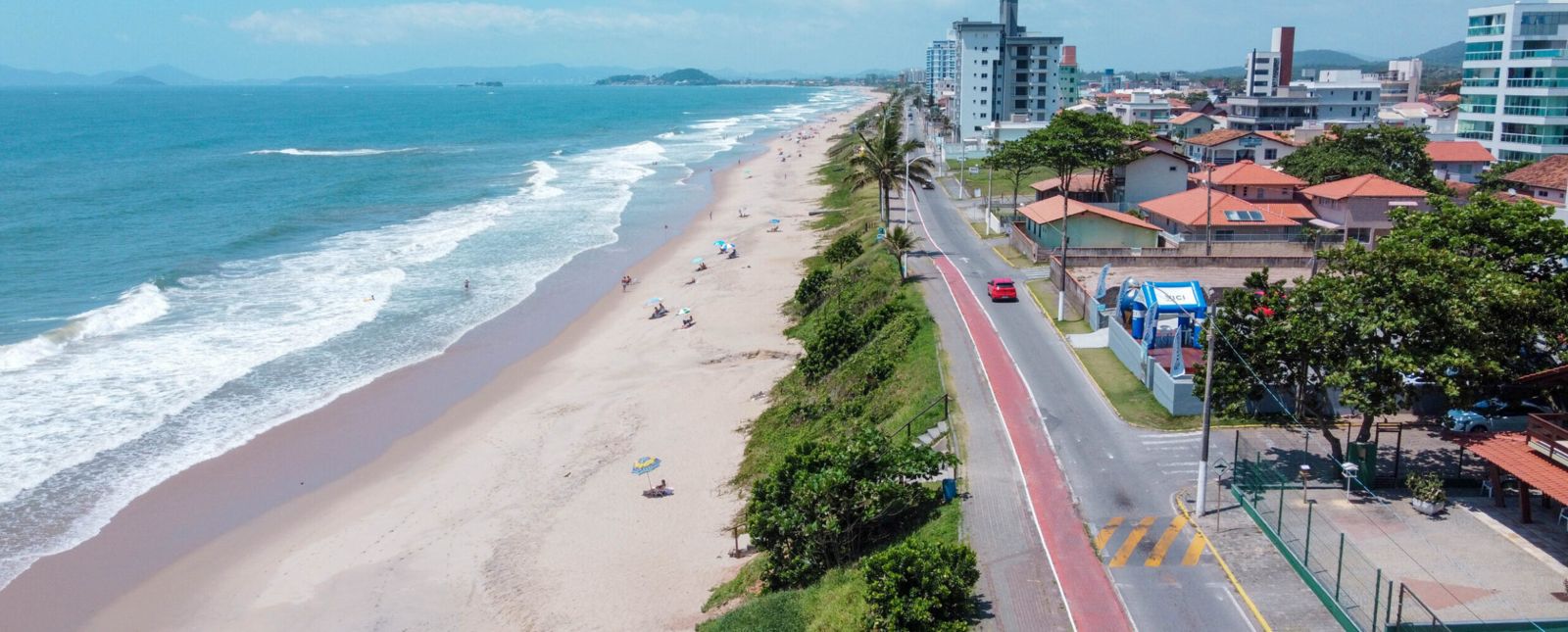 Vista aérea de Barra Velha atualmente, com orla movimentada, ciclovia à beira-mar e prédios próximos à praia