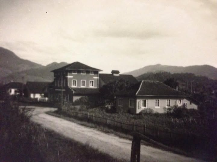 Casarão do antigo Salão Doering em foto antiga, com rua de chão e morros ao fundo, em Jaraguá do Sul
